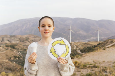 Woman holding light bulb and recycling symbol drawing at wind farm