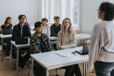 Multiracial students listening to teacher in classroom