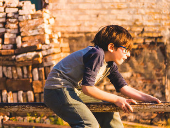 Side view of boy sitting on railing against brick wall