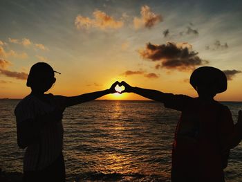 Silhouette people making heart shape while standing at beach during sunset