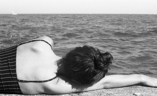 Rear view of woman lying on retaining wall by sea