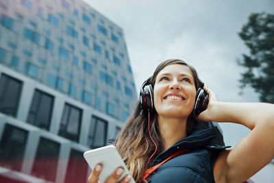 Smiling young woman with headphones and cell phone in the city