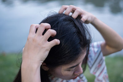 Close-up of woman scratching head by lake in park