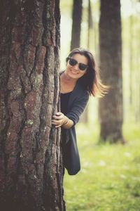 Portrait of smiling young woman holding tree trunk
