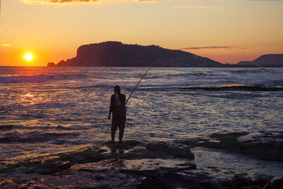 Rear view of silhouette man fishing in sea at sunset