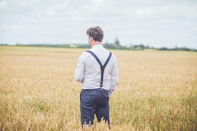 Rear view of man standing on field against sky