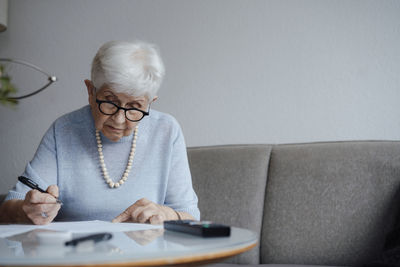 Senior woman doing paperwork sitting on sofa at home