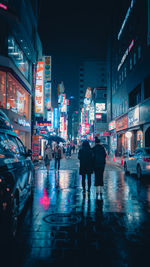 People walking on wet road in city at night