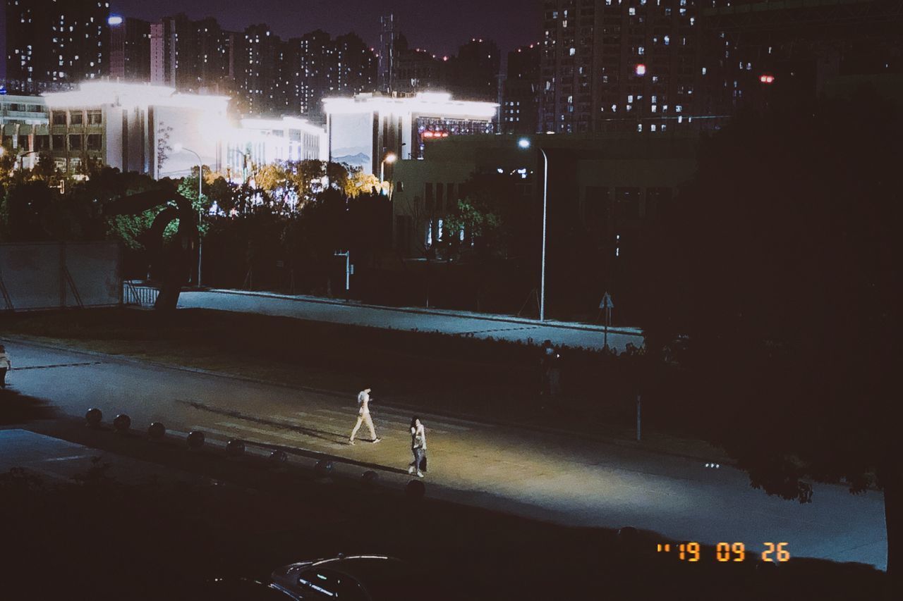 GROUP OF PEOPLE WALKING ON ROAD ALONG BUILDINGS AT NIGHT