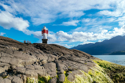 Lighthouse on rock by building against sky