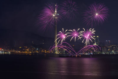 Firework display over illuminated city against sky at night