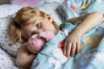 Portrait of cute baby girl with stuffed toy lying on bed at home