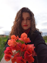 Portrait of young woman with red flowers against sky