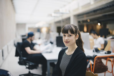 Portrait of confident computer programmer at office with colleagues working in background