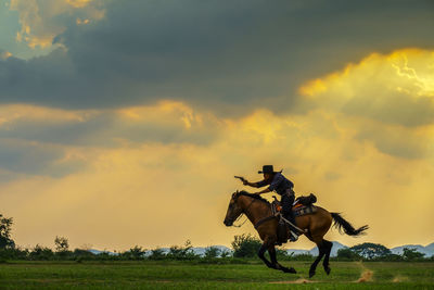 Horse riding motorcycle on field against sky during sunset