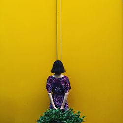 Rear view of man standing against yellow wall