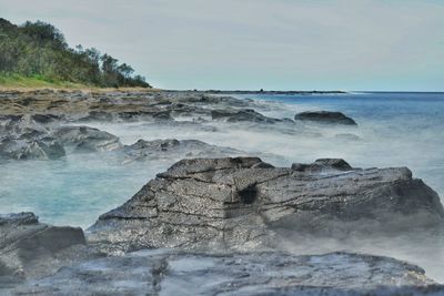 Scenic view of rocks on shore against sky