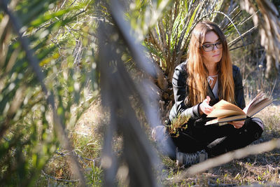 Close-up of teenager reading book while sitting on field