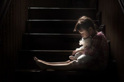 Cute girl looking down holding stuffed toy sitting on staircase at home