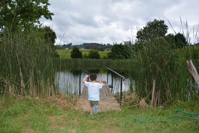 Rear view of boy walking on grassy field leading towards pond