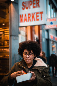 Woman eating food while standing against supermarket