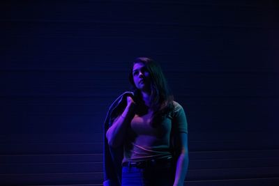 Woman holding jacket while standing against wall at night
