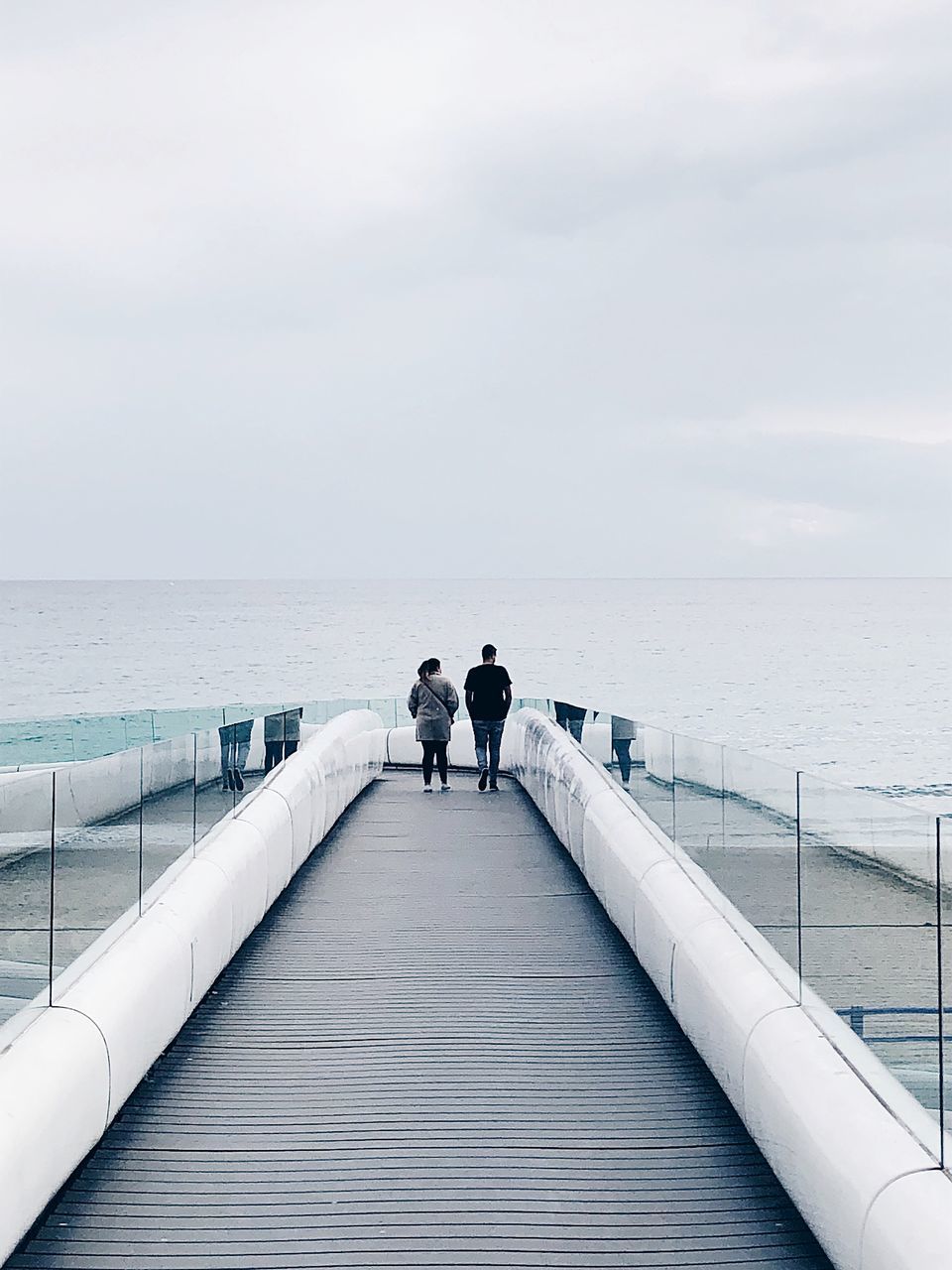 REAR VIEW OF MAN AND WOMAN LOOKING AT SEA