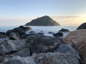 Rocks on beach against sky during sunset