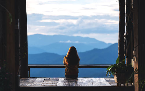 Rear view image of a female sitting and looking at a beautiful mountain and nature view