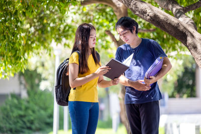 A couple of thai high school students smile while going through the woods with a book in their hand