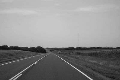 Country road amidst field against sky