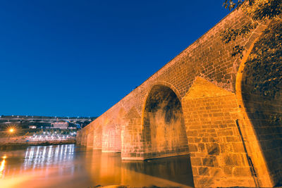 Arch bridge over river in city against clear sky