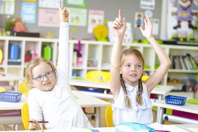Girls with hands raised at table in classroom