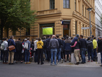 Rear view of people standing on street in city screening football
