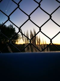 Close-up of chainlink fence against sky during sunset