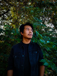 Young man looking away while standing in forest