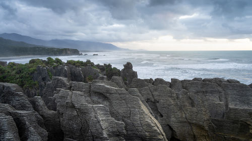 Sunset over rough ocean coast with big waves and pancake like rocks in foreground, new zealand