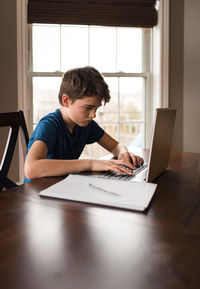 Tween boy working on his homework on a laptop commuter at home.