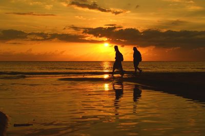 Silhouette people walking at beach against sky during sunset