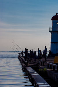 People on pier by sea against sky during sunset