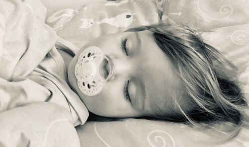 High angle view of girl with pacifier sleeping on bed