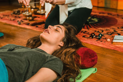 Low section of therapist holding bells by young woman while performing music therapy at spa