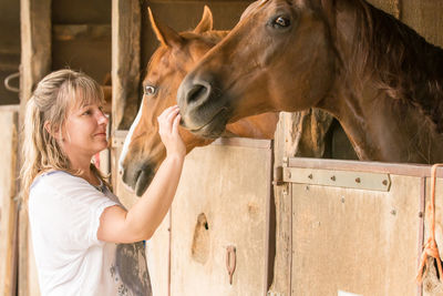 Side view of woman petting horse in stable
