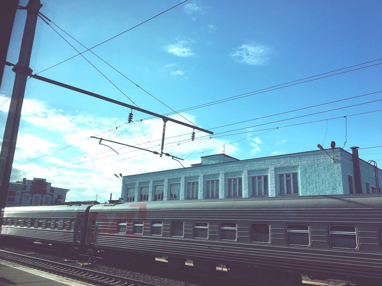 transportation, cable, railroad track, rail transportation, sky, public transportation, power line, train - vehicle, cloud - sky, mode of transport, day, railroad station, railroad station platform, built structure, outdoors, power supply, electricity pylon, no people, architecture, building exterior, commuter train