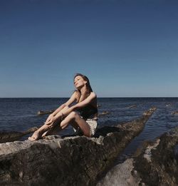 Woman sitting on rock by sea against clear sky