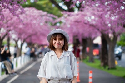Portrait of smiling woman standing by pink flower trees
