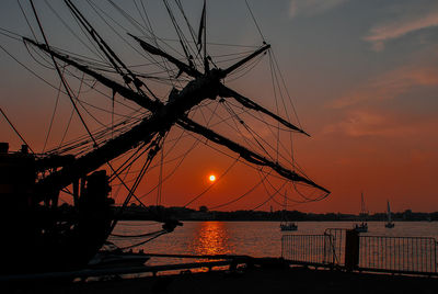 Silhouette sailboat moored at harbor against sky during sunset