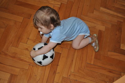 High angle view of boy playing with soccer ball on hardwood floor at home