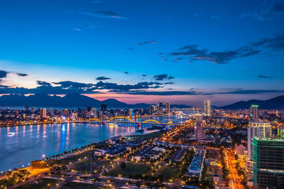 Aerial view of river amidst illuminated buildings in city at night