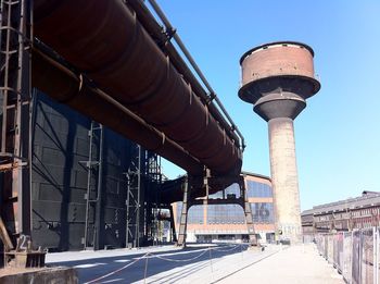 Low angle view of large pipes and industrial water tower against clear sky